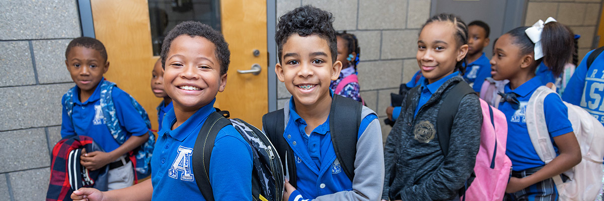 Group of smiling students wearing backpacks pose together in a hallway